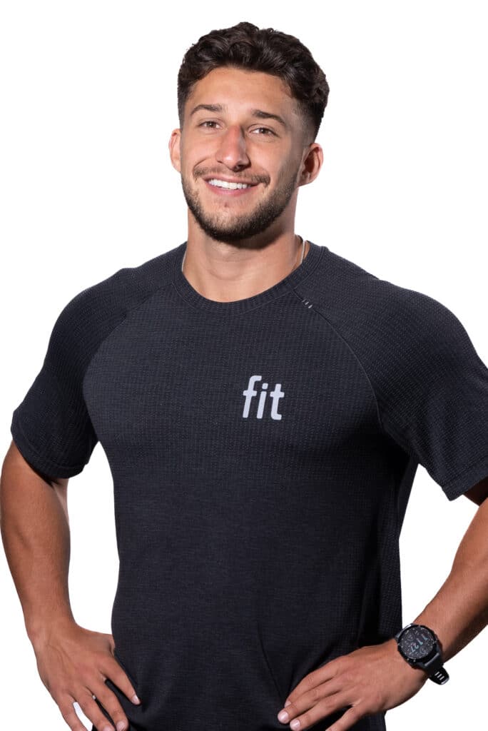 A man with a beard and short hair is smiling and wearing a black t-shirt with the word "fit" on it. He has his hands on his hips and is wearing a watch on his left wrist.