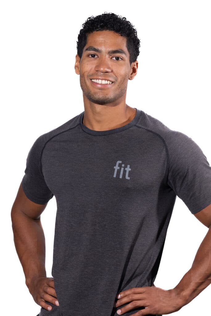 A man with curly hair wearing a gray athletic shirt with the word "fit" on it, smiling with his hands on his hips.