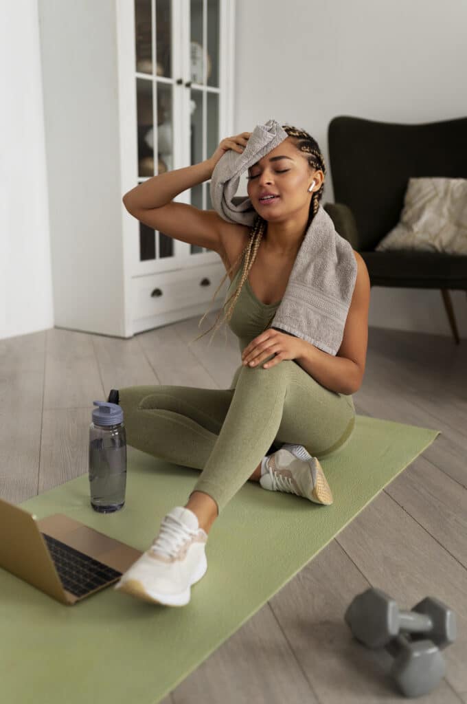A woman sitting on a yoga mat with a towel on her head and a laptop on her lap.