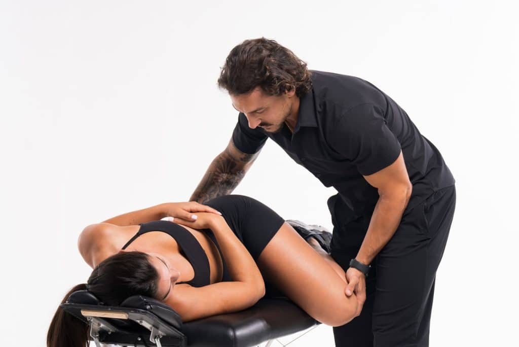 A physical therapist, dressed in black attire, assists a woman lying on her side on a treatment table during a therapy session.