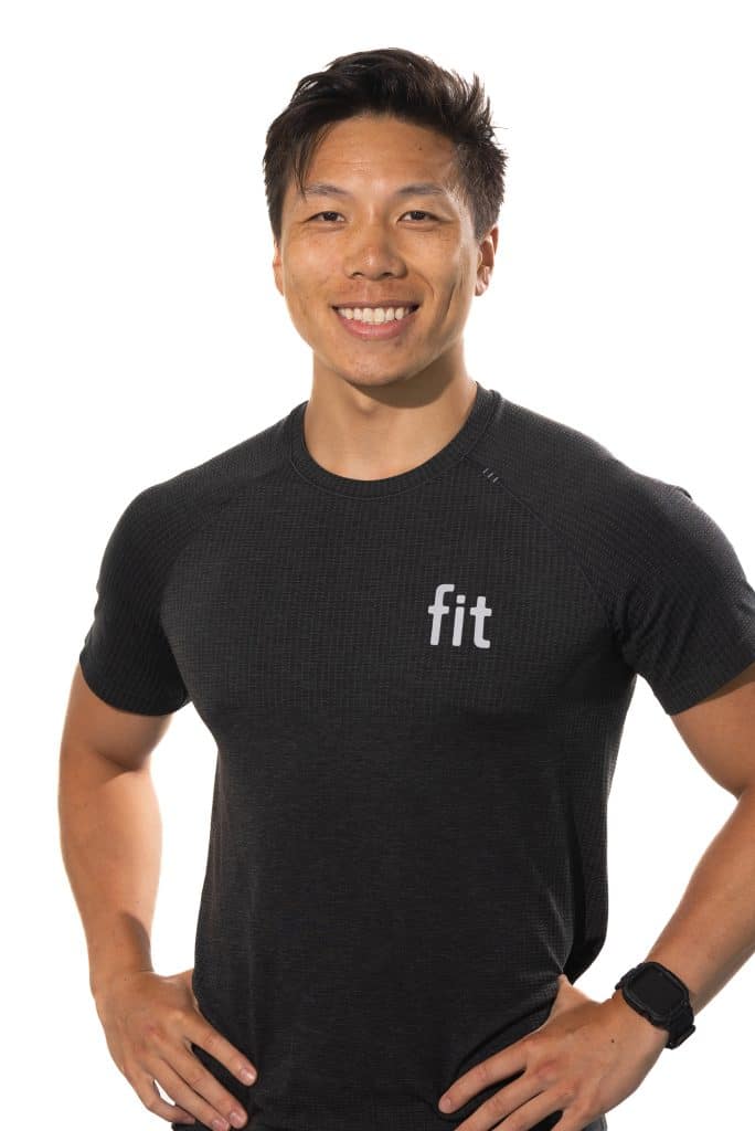 A person in a black "fit" shirt smiling with hands on hips against a white background.