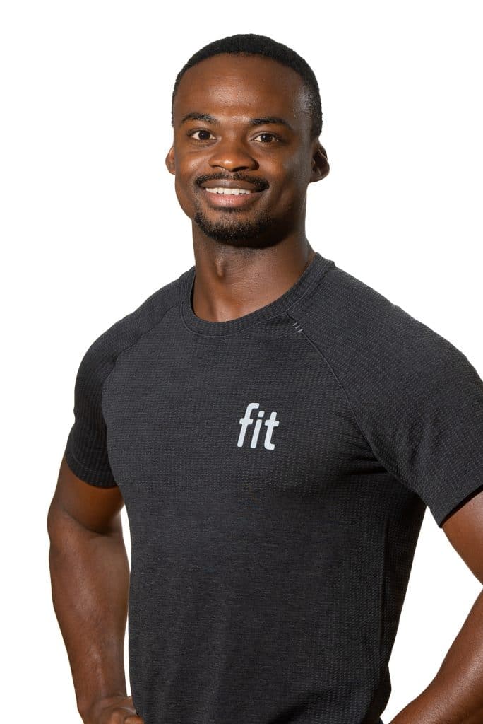 A person wearing a dark t-shirt with "fit" written on it smiles with hands on hips against a plain background.